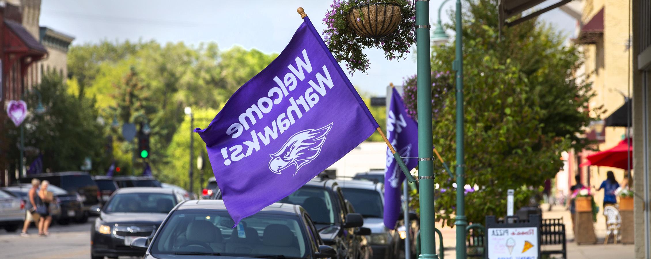 A purple flag that says welcome Warhawks hangs off a business in downtown Whitewater.